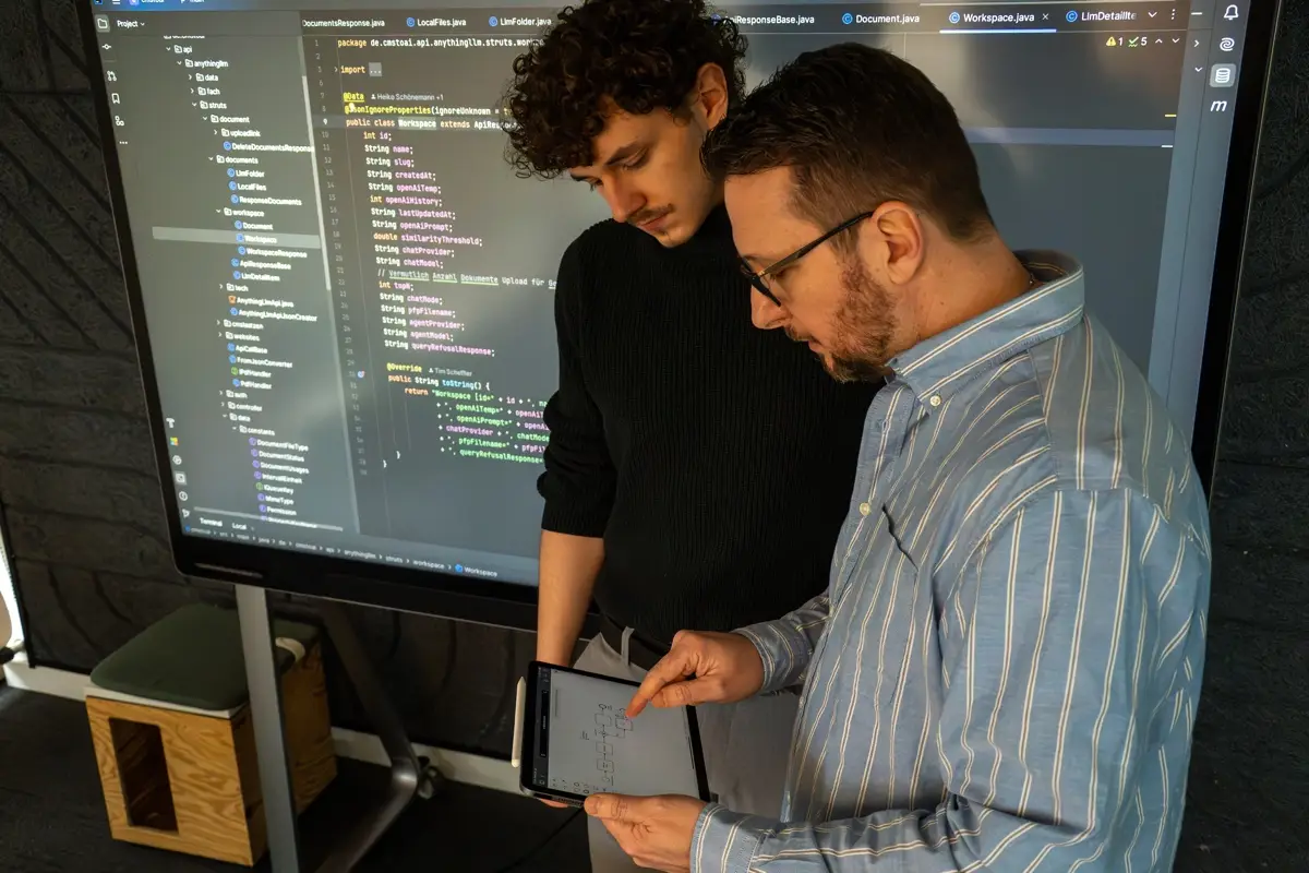 Heiko Schönemann bespricht mit einem Entwickler Code auf einem großen Bildschirm